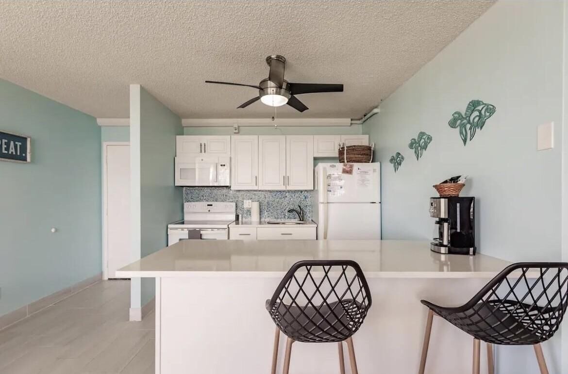 A modern kitchen with white cabinets, a central island, and two black chairs.