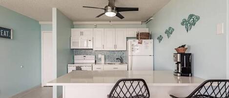 A modern kitchen with white cabinets, a central island, and two black chairs.