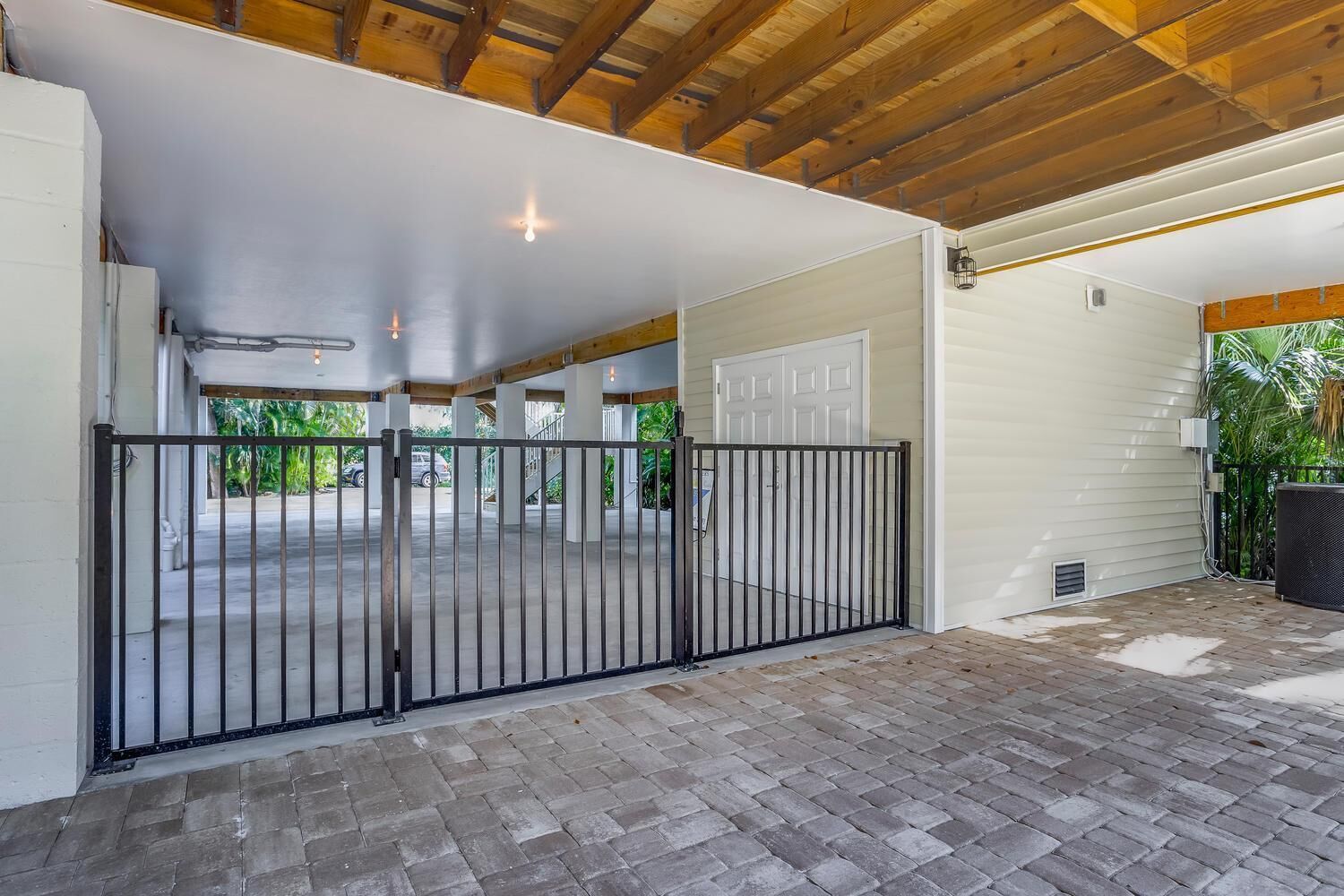 A covered parking area with a gated entrance, a concrete floor, and a white exterior wall.