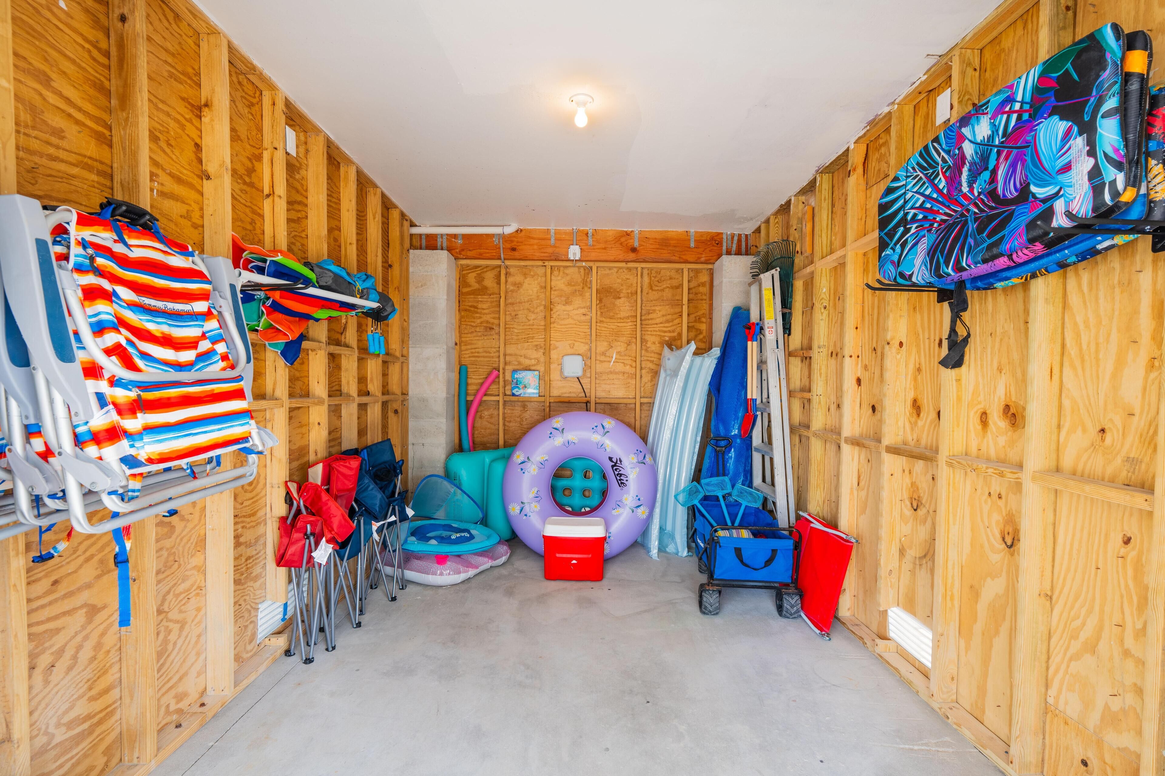 A room with wooden walls, a ceiling light, a colorful mat, a purple inflatable ring, a red cooler, and a blue cart.