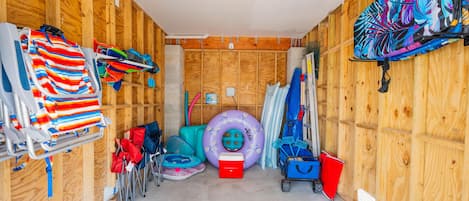 A room with wooden walls, a ceiling light, a colorful mat, a purple inflatable ring, a red cooler, and a blue cart.
