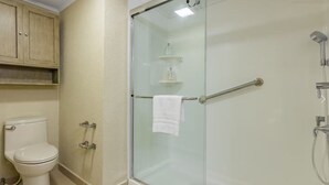 A bathroom with a glass-enclosed shower, a toilet, and a wooden cabinet above the toilet.