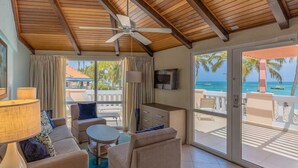 A room with a ceiling fan, a TV, a sofa, a coffee table, and a view of the ocean.