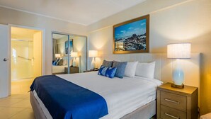 A hotel room with a large bed, bedside lamps, a nightstand, a mirror, and a painting on the wall.