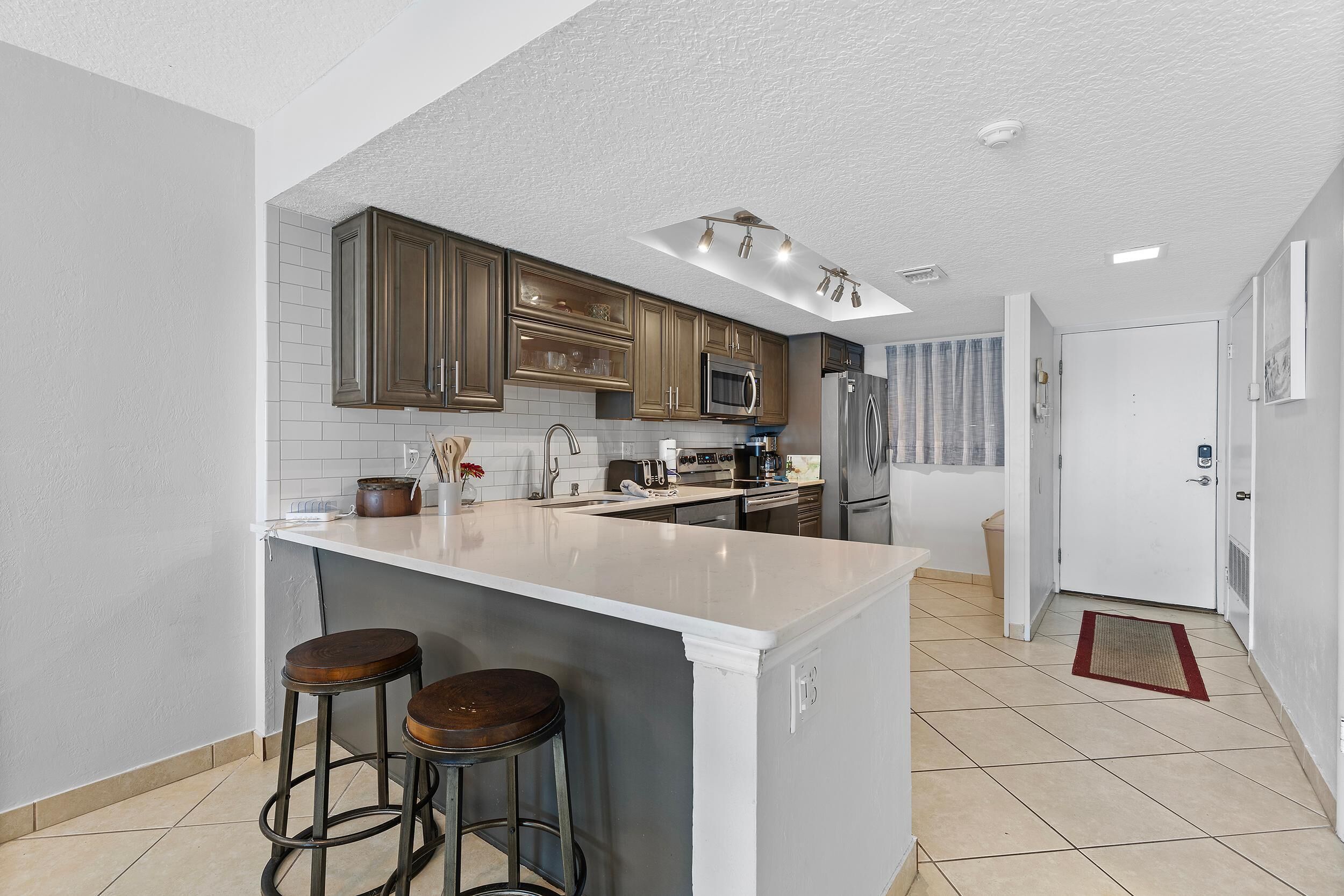 Una cocina moderna con una isla central, taburetes de bar y un microondas.