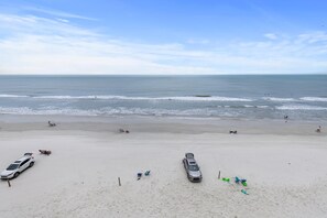 A wide sandy beach with a few parked cars and people in the distance. - Ponce de Leon Towers 503 (New Smyrna Beach)