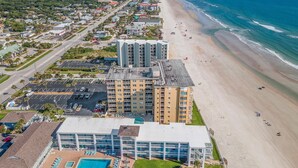 An aerial view of a coastal hotel with multiple buildings, a beach, and a clear view of the ocean. - Ponce de Leon Towers 702 (New Smyrna Beach)