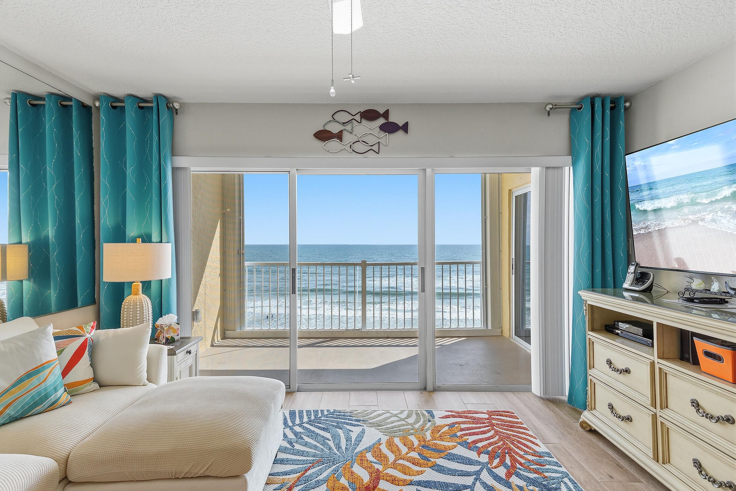 A room with a view of the beach, a sofa, a TV, and a desk with drawers.