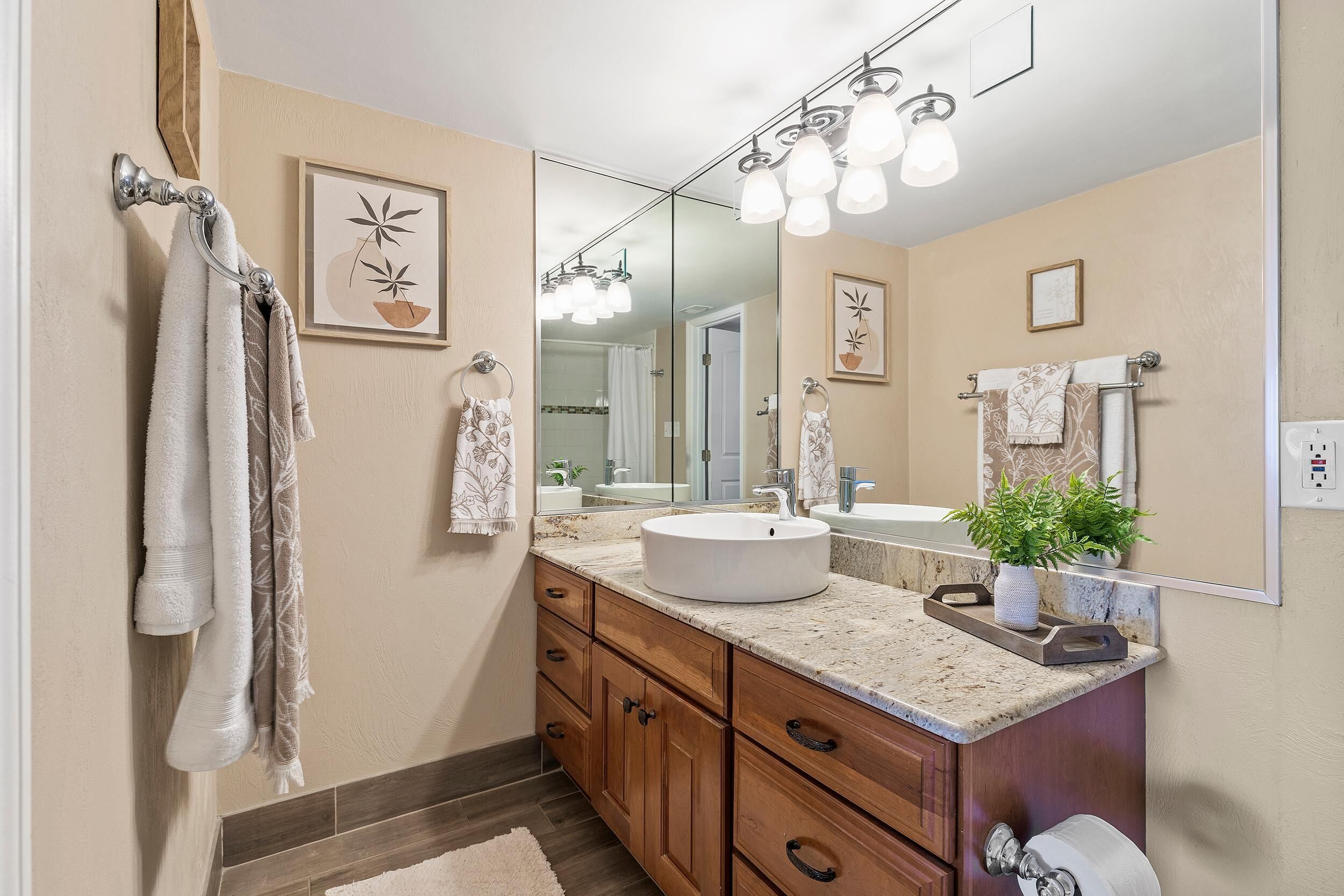 A bathroom with a large mirror, a sink, wooden cabinets, and towels hanging on a rack.