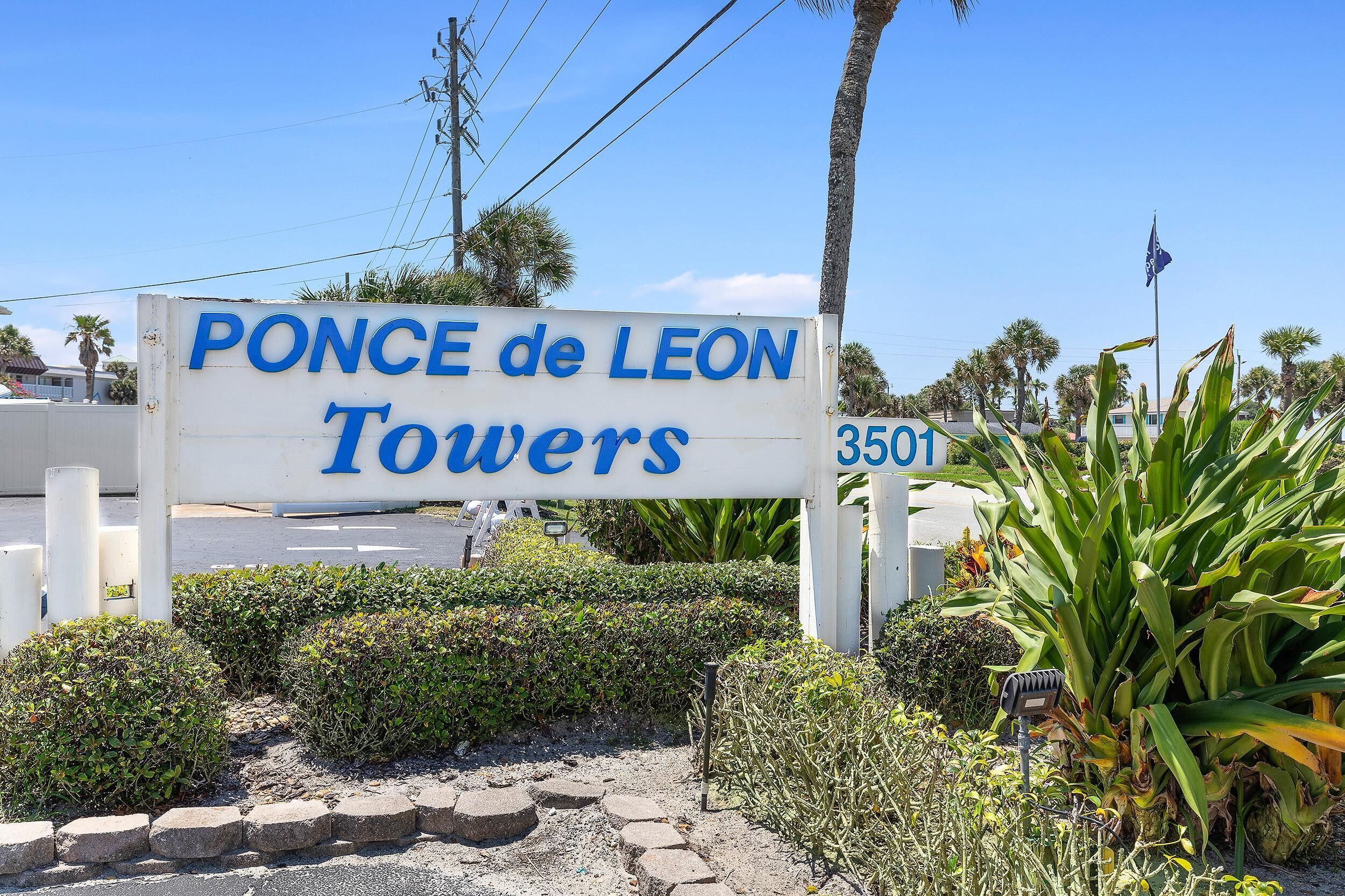A sign for "Ponce de Leon Towers" with a clear view of the surrounding landscaping and a street in the background.