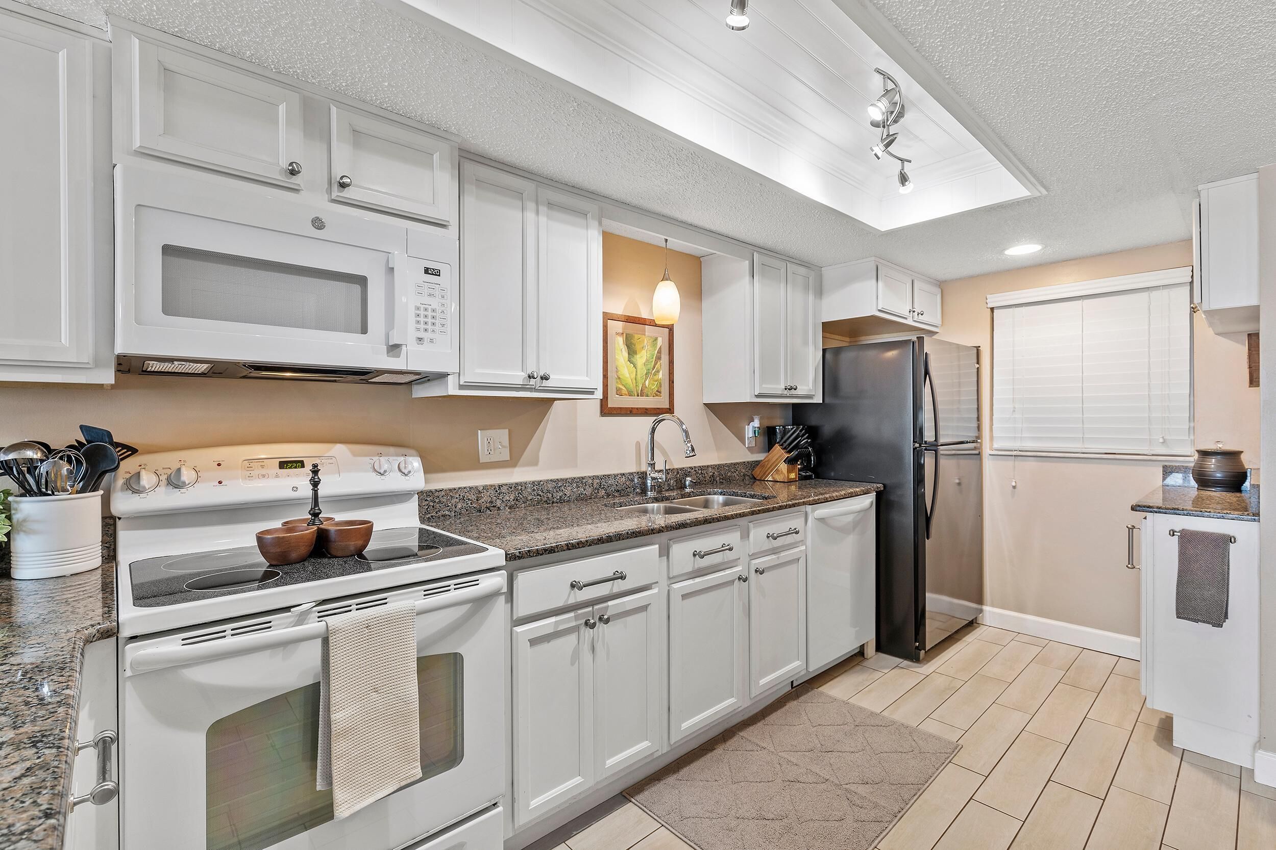 A modern kitchen with white cabinets, a granite countertop, a stainless steel refrigerator, and a built-in oven.