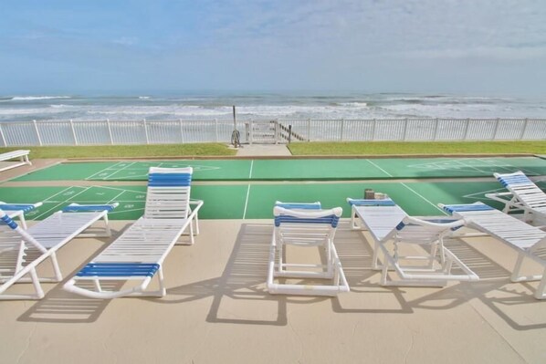 A deck with lounge chairs and a shuffleboard table, overlooking the ocean.
