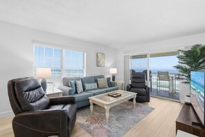 A modern living room with a sofa, two armchairs, a coffee table, and a large window offering a view of the ocean.