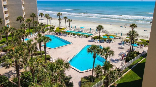 A resort with two swimming pools, a beach, and palm trees. - Pelican C606 (New Smyrna Beach)