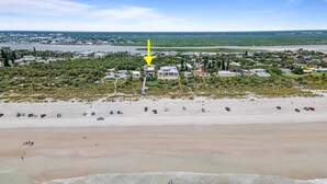 Une vue aérienne d’une plage bordée d’une rangée de maisons, d’un rivage sablonneux et d’une mer calme.