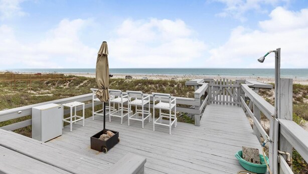 Une terrasse en bois avec des chaises blanches et une table, donnant sur une plage.
