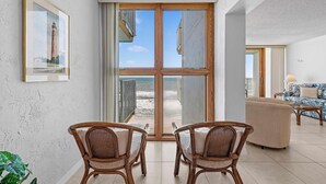 Una habitación con un gran ventanal corredizo que da a la playa, dos sillones de mimbre, un sofá y un cuadro en la pared.