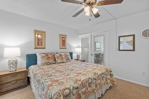 A bedroom with a bed, two bedside lamps, a ceiling fan, and framed pictures on the walls. - Smyrna Beach Club 607a (New Smyrna Beach)