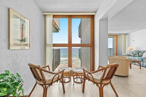 A modern living room with a large glass door leading to a balcony overlooking the sea, wicker furniture, and a framed picture on the wall. - Smyrna Beach Club 607a (New Smyrna Beach)