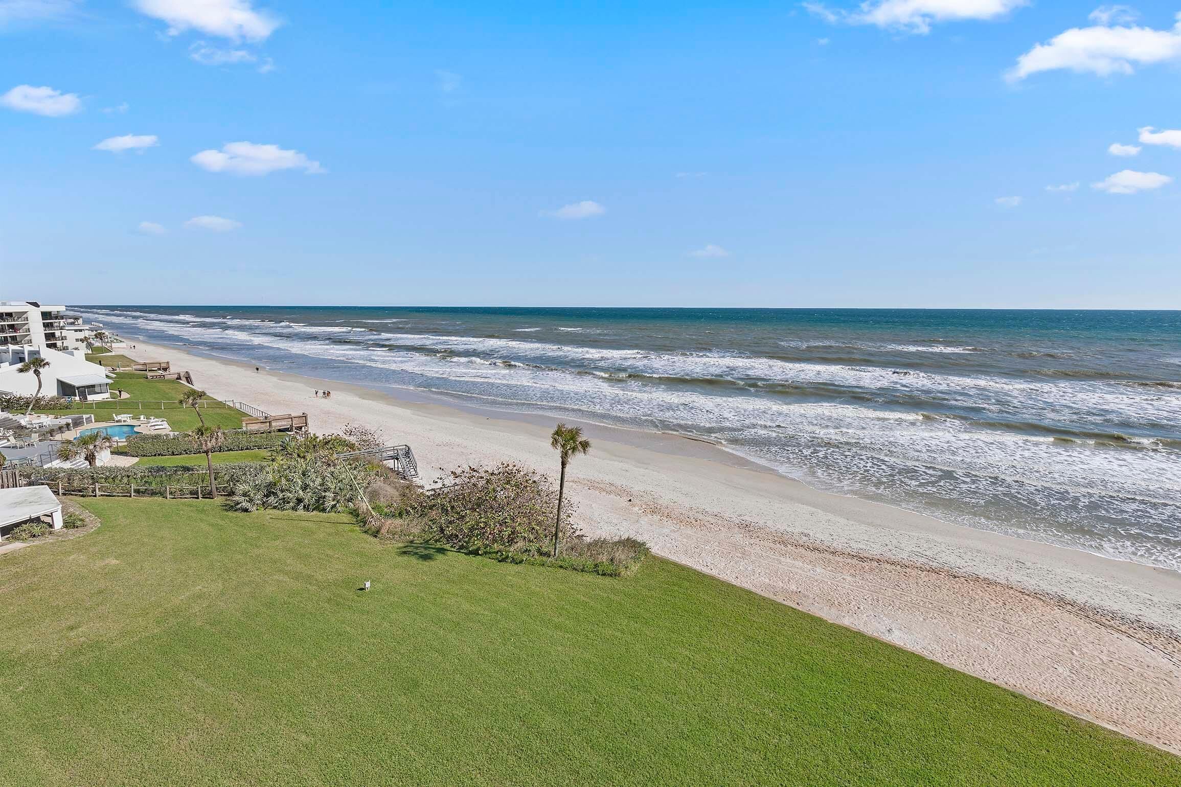 Vista de una playa con zona verde, piscina y un edificio de varios pisos.