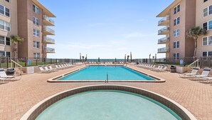 Un espace piscine comprenant une piscine rectangulaire et un petit jacuzzi rond, le tout entouré de chaises longues et de palmiers.