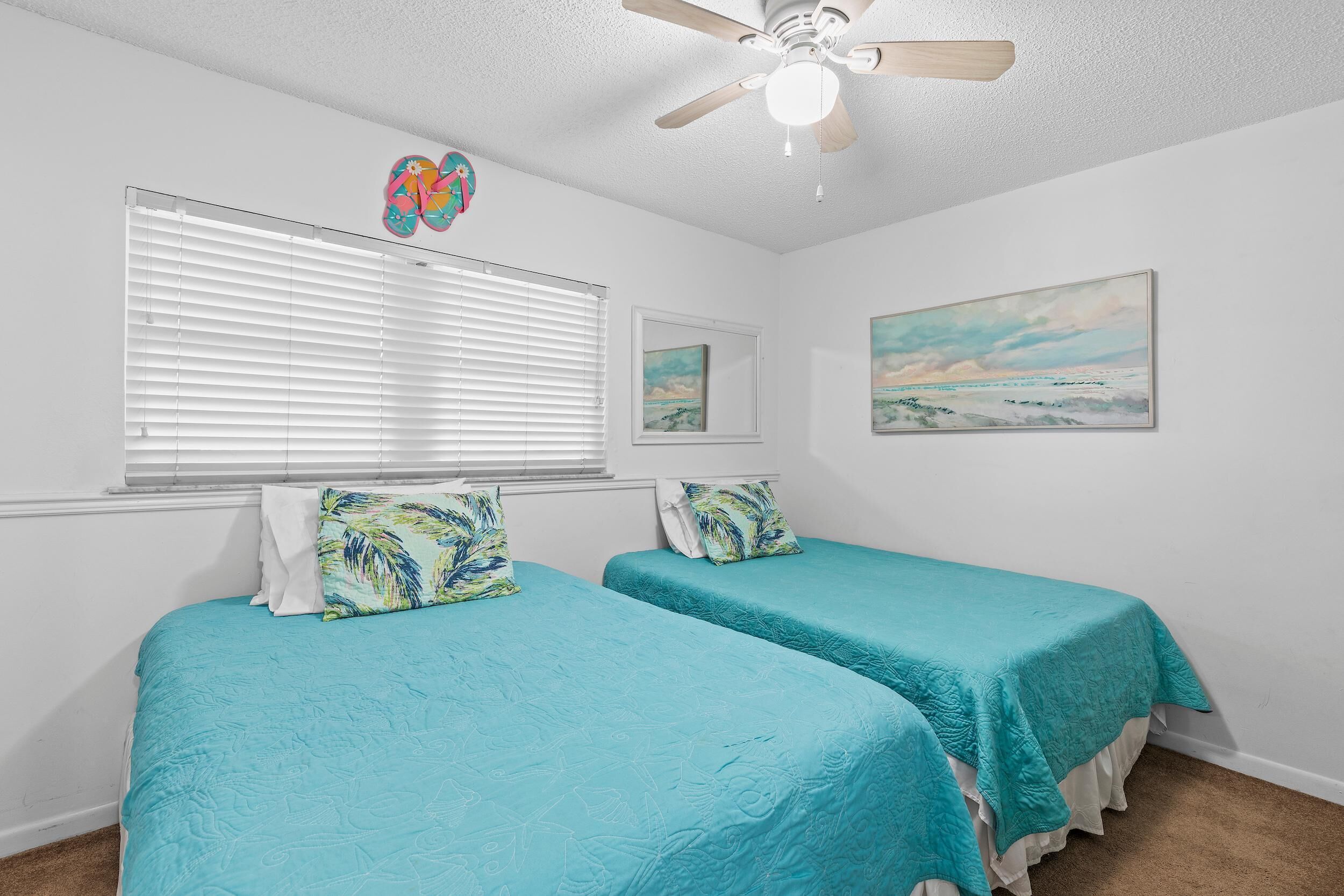 A bedroom with two beds, a ceiling fan, and a window with blinds.