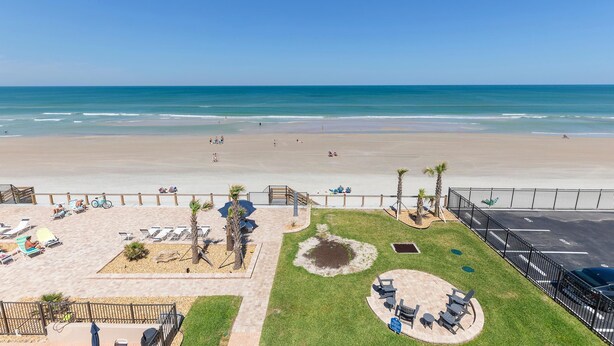 Une vue sur la plage avec un espace patio comprenant des chaises longues, un barbecue et un petit jardin.