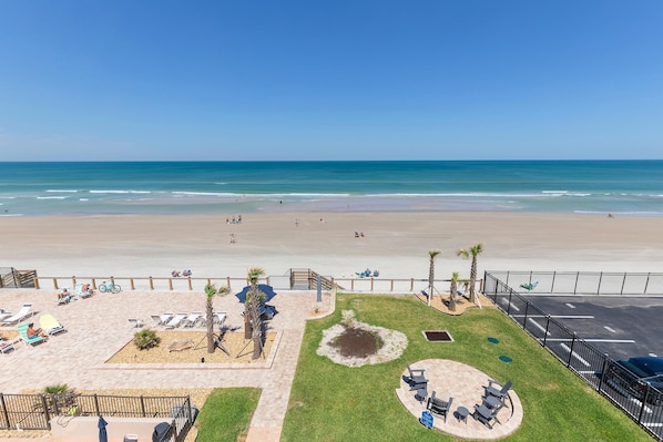 Enjoy the ocean view from our beachfront patio with lounge chairs and umbrellas, surrounded by a small garden with palm trees.