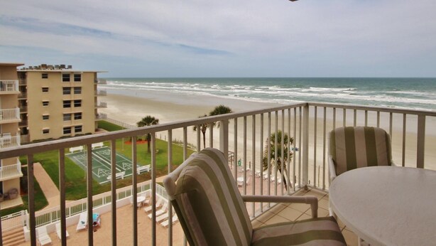 Ein Balkon mit Blick auf Strand und Meer. Zwei Stühle und ein Tisch sind vorhanden.