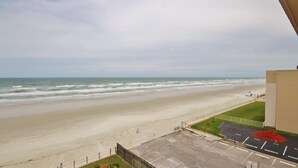 Blick auf einen Strand vom Balkon, im Vordergrund ein Parkplatz.