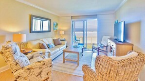 Ein Wohnzimmer mit Sofa, Sesseln, Couchtisch, Fernseher und einem Balkon mit Blick.
