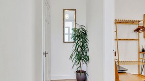 A hallway with a potted plant, a mirror, and a wooden shelf unit.