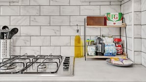 A kitchen with a gas stove, a shelf with various food items, and a tiled backsplash.