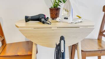 Une table ronde en bois sur laquelle se trouvent un pot de fleurs, un sèche-cheveux et un appareil blanc.