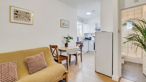 A modern kitchen with white cabinets, a dining area with a beige sofa and patterned cushions, and a small dining table with chairs.