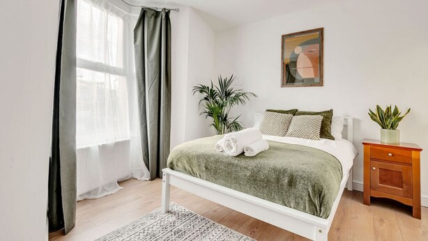 A bedroom with a bed, a nightstand, a potted plant, and a painting on the wall.