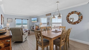 Un coin repas avec une table et des chaises en bois, un lustre et une décoration murale sur le thème de la plage.