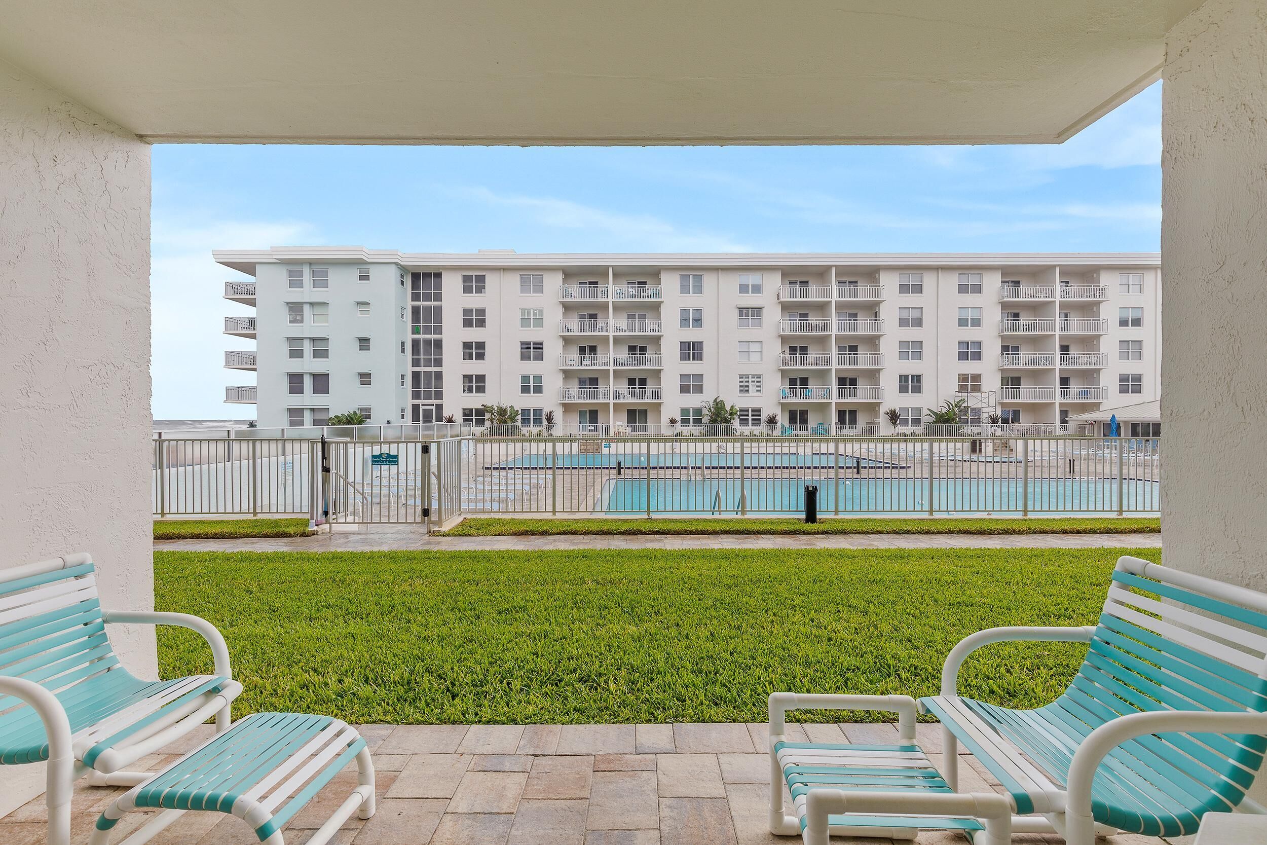 A balcony with two green and white striped benches, a swimming pool, and a multi-story building in the background.