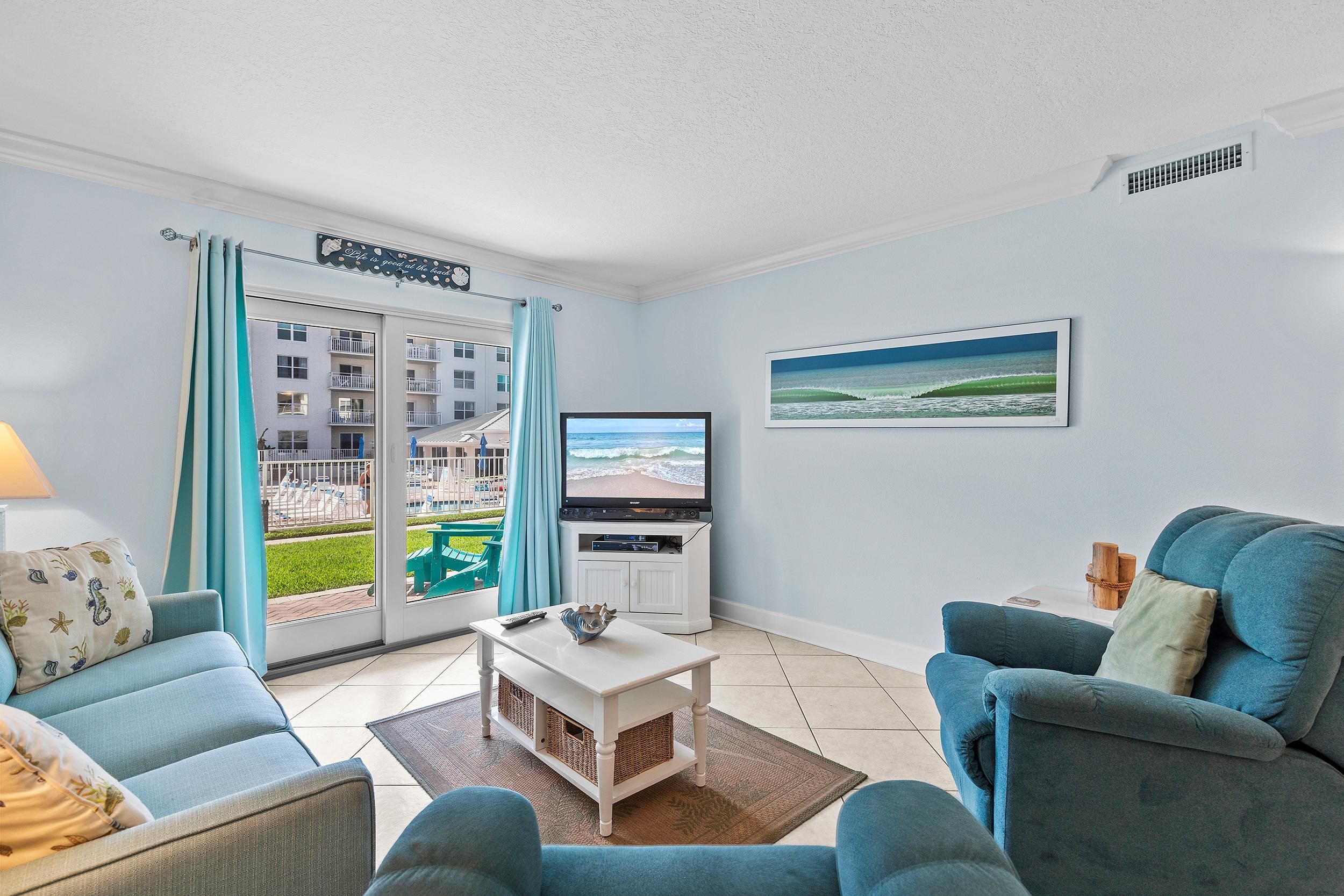 A living room with a TV, a sofa, a chair, and a view of a building with balconies.