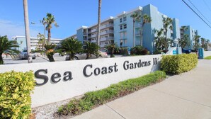 A sign for Sea Coast Gardens II with a multi-story building in the background. - Sea Coast Gardens II 307 (New Smyrna Beach)