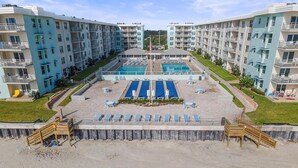 A hotel with multiple floors, a swimming pool, and outdoor seating areas. - Sea Coast Gardens II 307 (New Smyrna Beach)