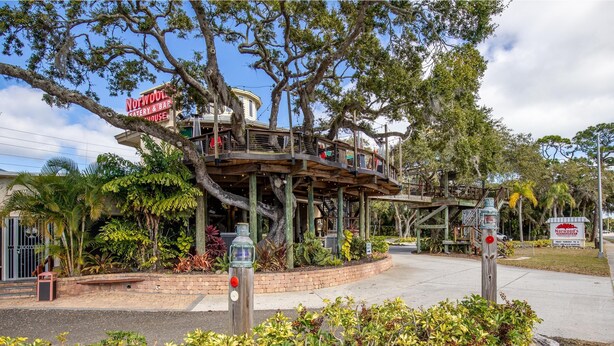 A treehouse restaurant with outdoor seating, surrounded by lush greenery and a clear sky. - Sea Coast Gardens II 307 (New Smyrna Beach)