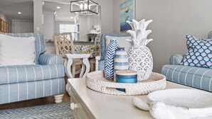 Una sala de estar con un sofá azul a rayas, una mesa de centro con objetos decorativos y una cocina al fondo.