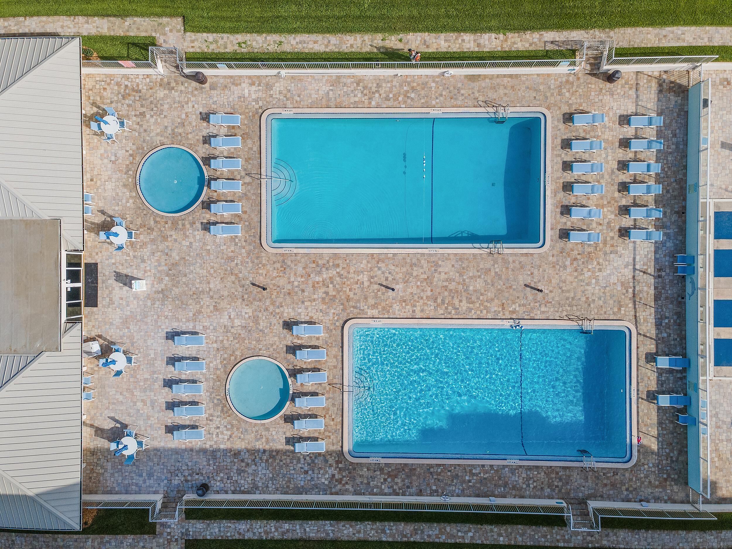 An aerial view of a pool area with two rectangular pools, surrounded by lounge chairs and tables.
