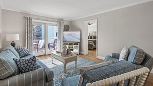Una sala de estar con sofá, una mesa de centro y televisor. Tiene un balcón con vistas a edificios.