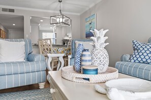 Een woonkamer met een blauw gestreepte bank, een salontafel met decoratieve objecten, en een keuken op de achtergrond.