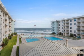 A hotel with a pool area, a view of the ocean, and a flag. - Sea Coast Gardens II 316 (New Smyrna Beach)