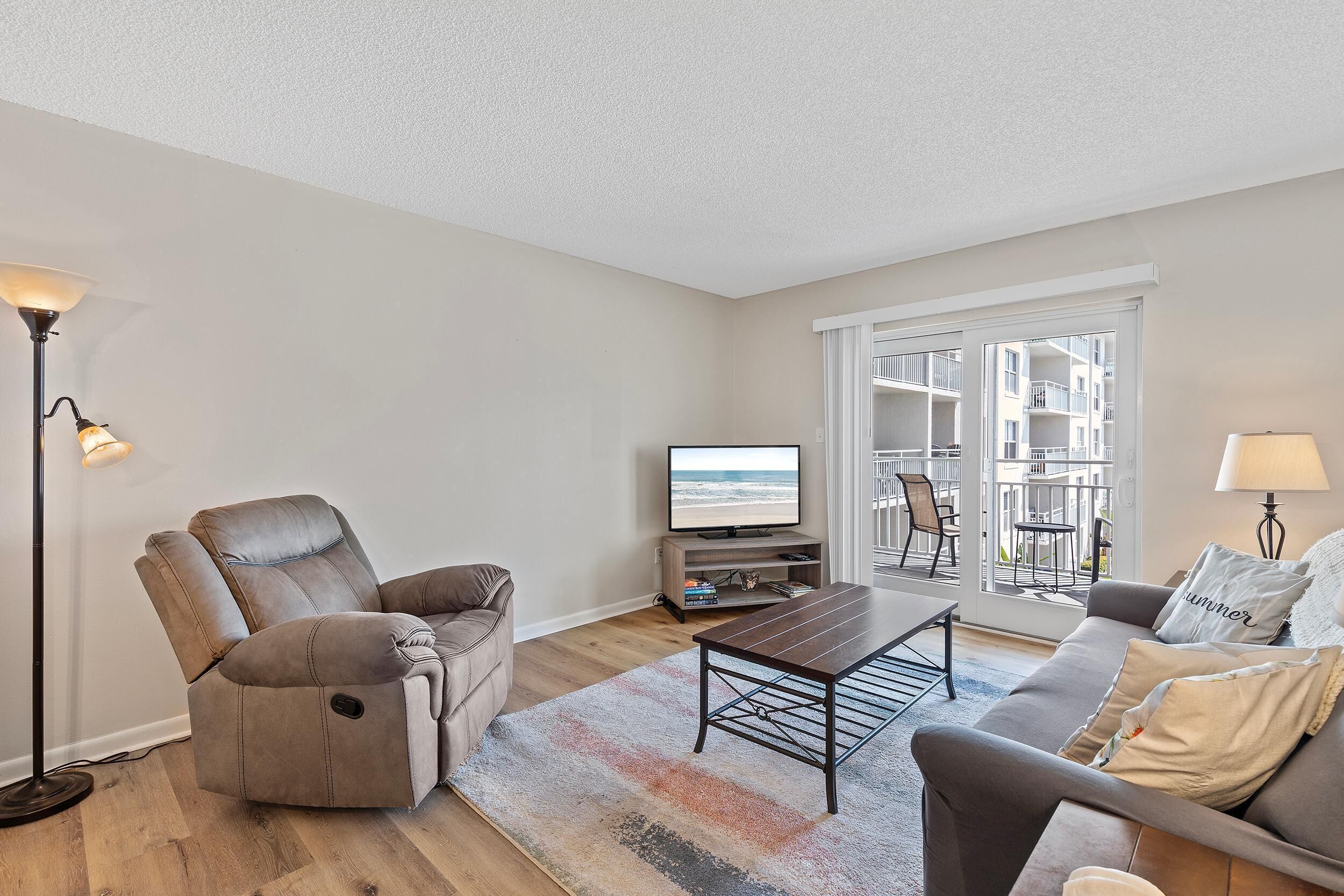 Ein Wohnzimmer mit Liege- und Sofa, einem Couchtisch, einem Fernseher und einem Balkon mit Gartenmöbeln.