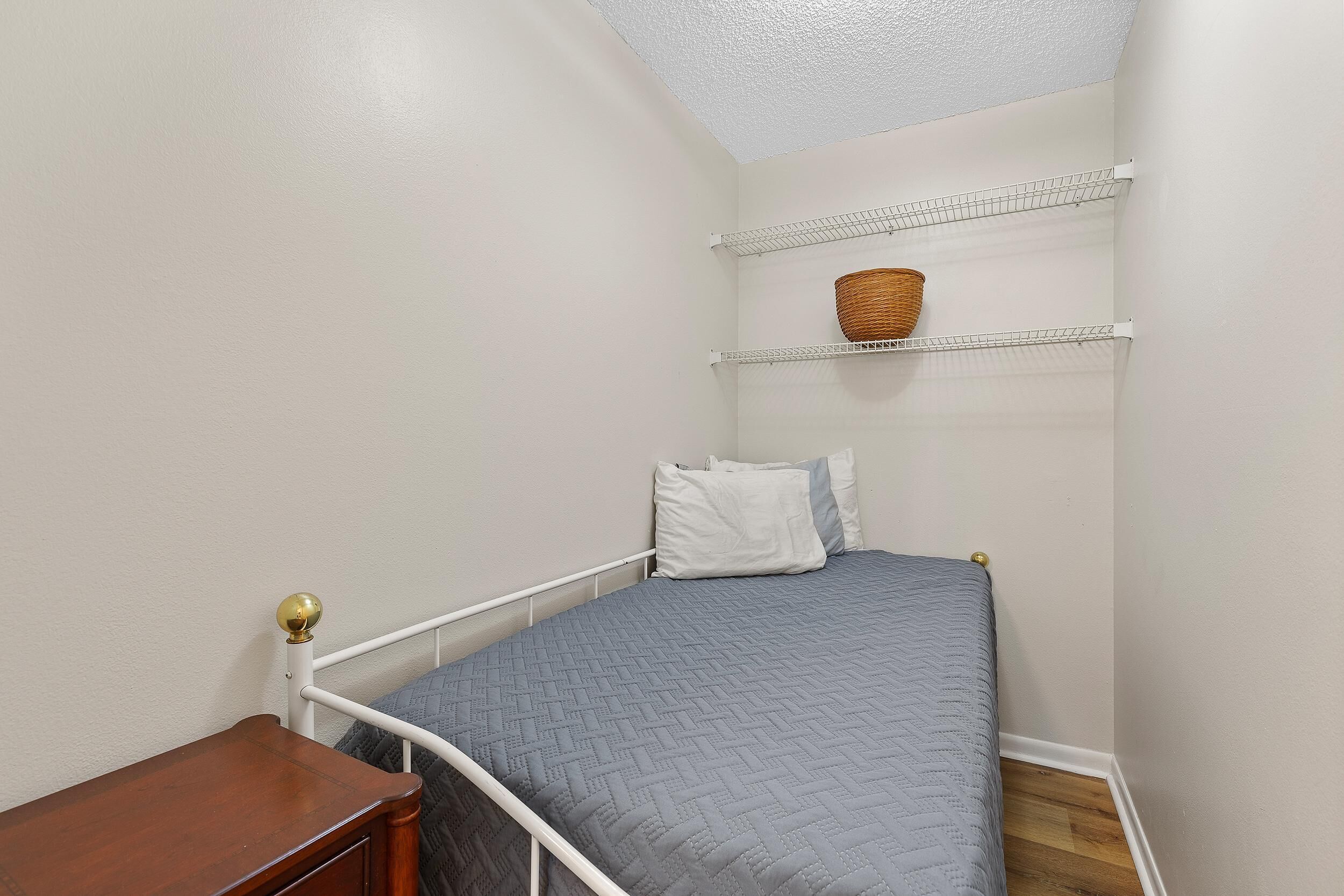 Un dormitorio pequeño y ordenado con una cama individual, una mesita de noche y una estantería con una cesta.