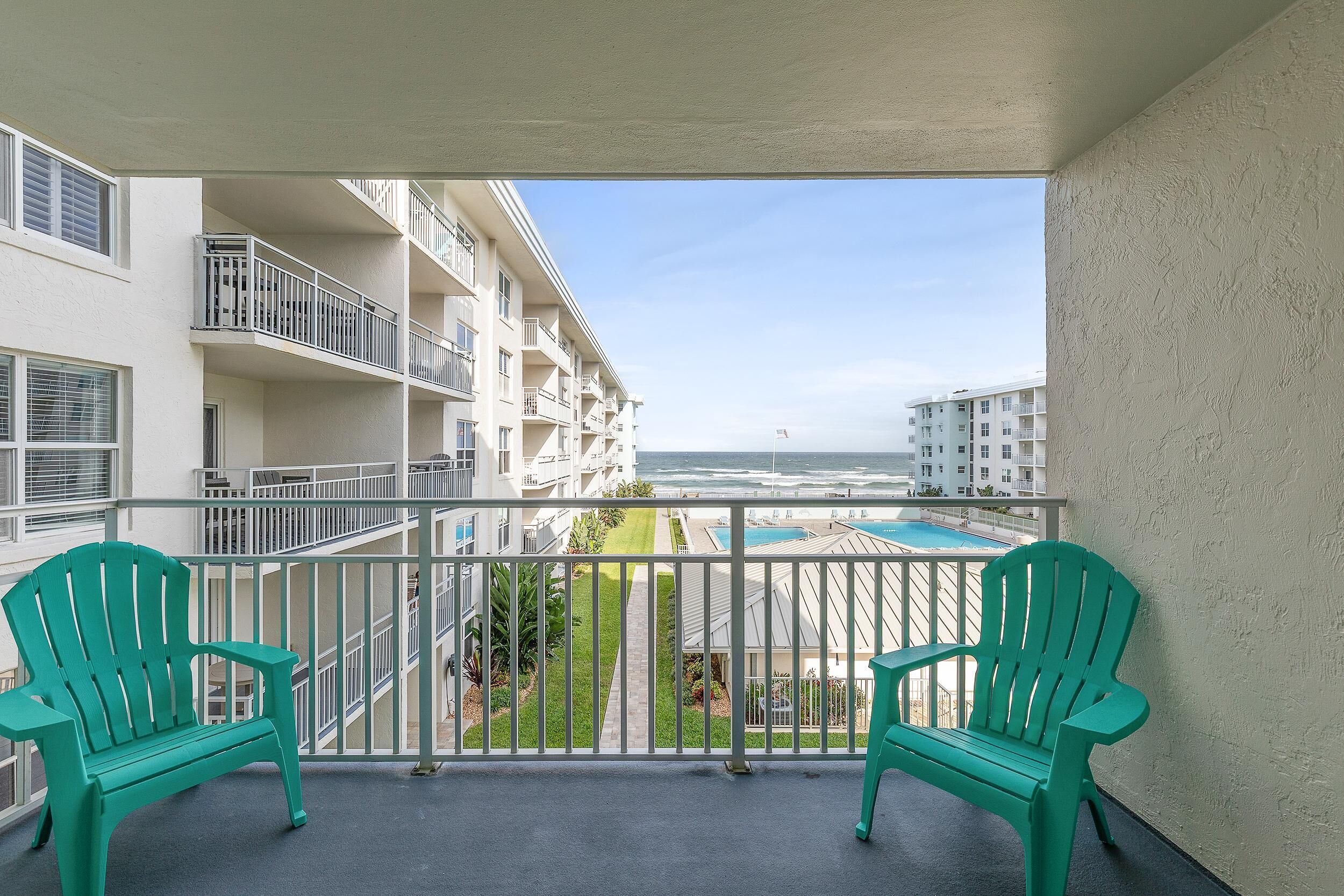 Ein Balkon mit zwei grünen Stühlen, Blick auf einen Pool und ein Gebäude mit mehreren Balkonen.